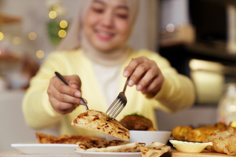 Closeup of Asian Muslim woman serving flatbread during Ramadan iftar meal at home. Warm dining moment highlights traditional cuisine, comfort food, and enjoyment of evening dishes shared during the holy month