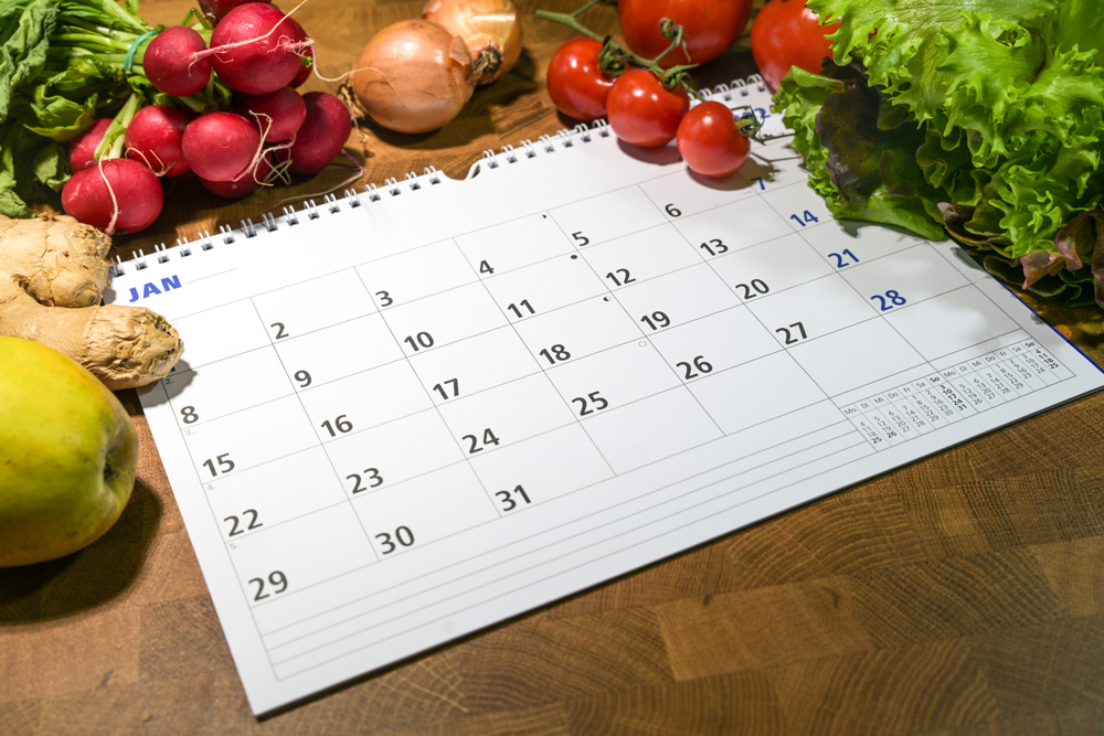Calendar with month of January surrounded by fresh vegetables and fruits on a wooden table, new year goals to eat healthy food and lose weight, copy space, selected focus, narrow depth of field