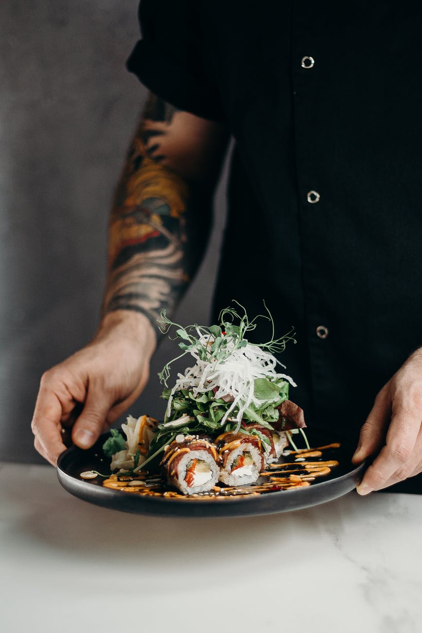 A person holding a plate full of tofu, vegetables, and sauce