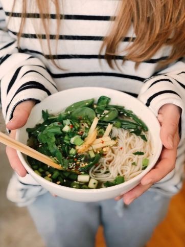 A person holding a bowl full of soup noodles