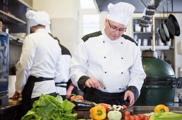 A chef in a kitchen about to cut various vegetables.