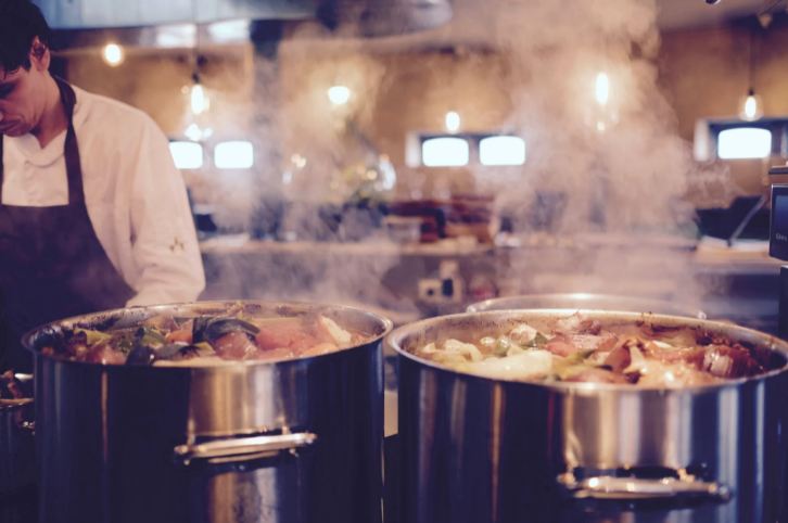 Man cooking soup in two large metal pots.