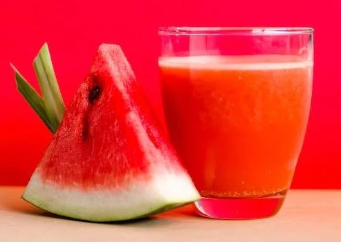 Watermelon shake filled glass cup beside sliced watermelon fruit on brown surface