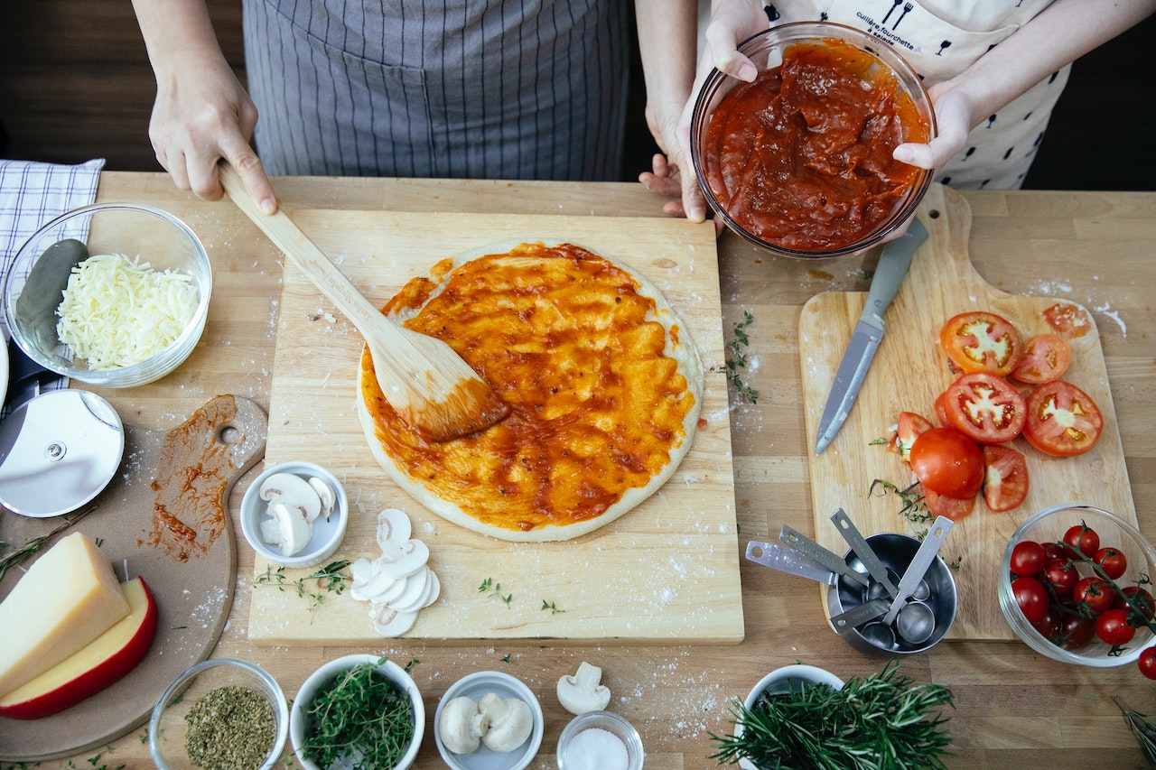 Photo crop women spreading tomato sauce on pizza