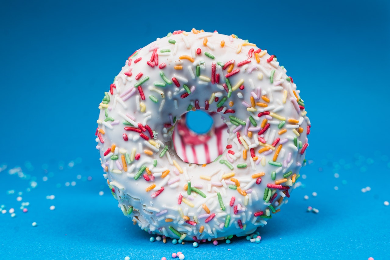A close-up photo of a white donut with colorful sprinkles