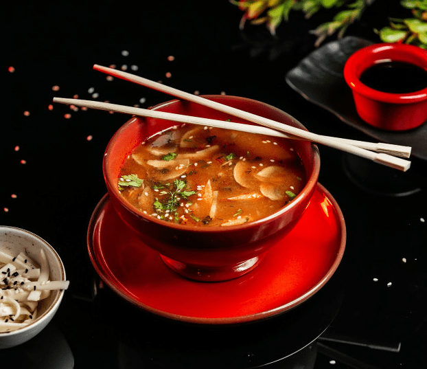 A bowl of miso soup with chopsticks on a table.
