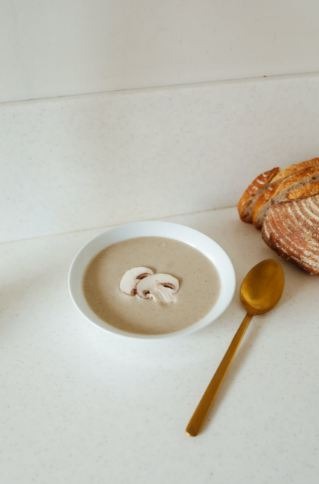 A bowl of mushroom soup with a golden spoon and some pieces of bread