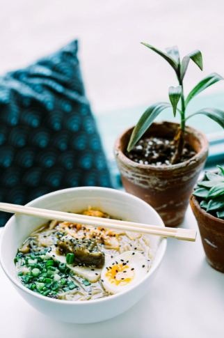 A  bowl of soup noodles on a table with some plants