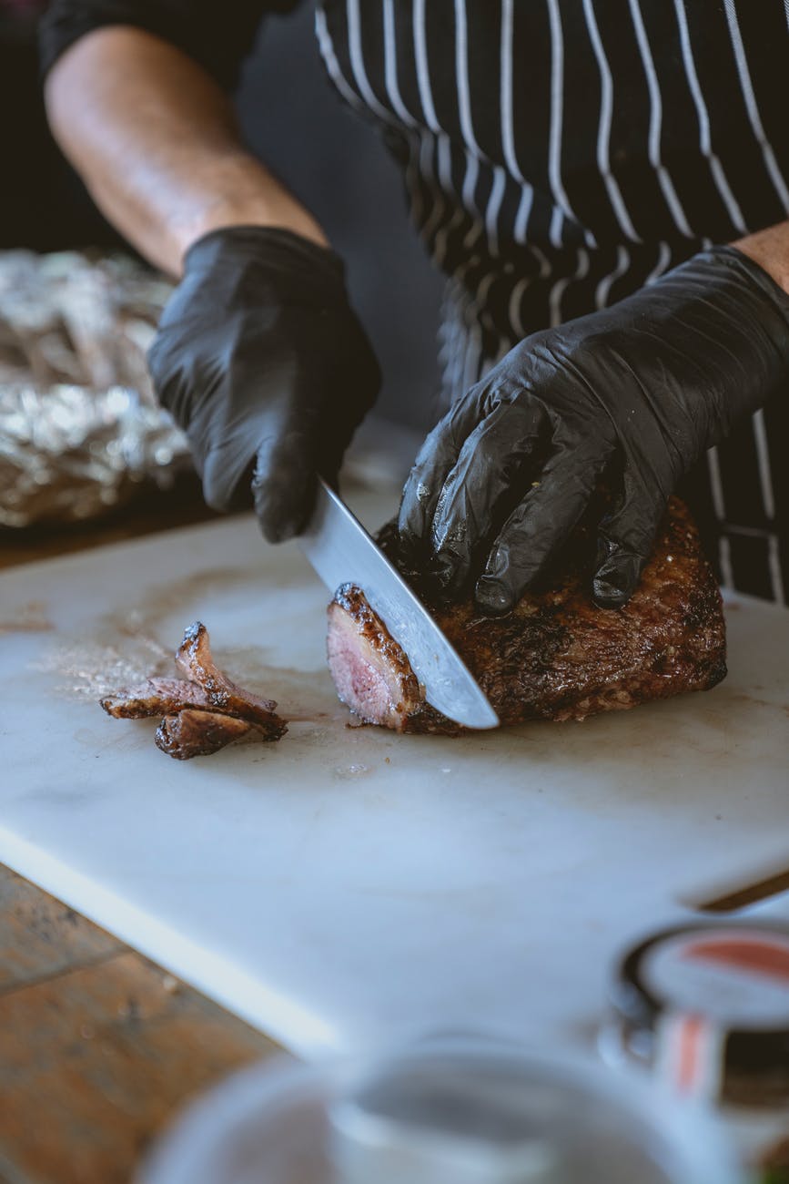 A person cutting a piece of beef into thin slices