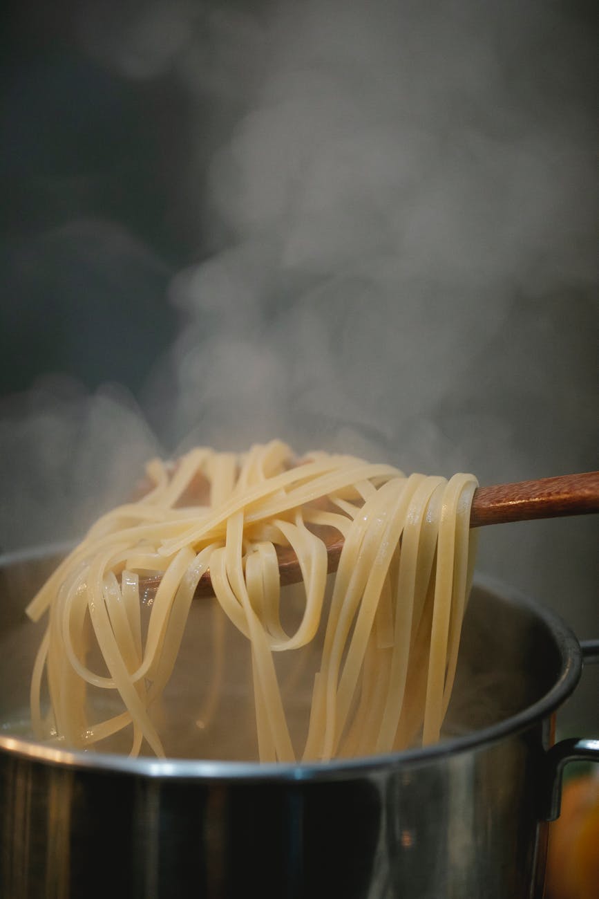 Noodles on a wooden spoon with steam coming out from the pan