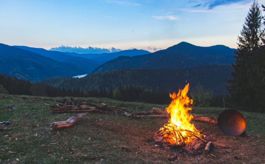 a bonfire at the mountains surrounded by a green grass field