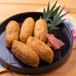 Inari sushi in a black bowl with a leaf