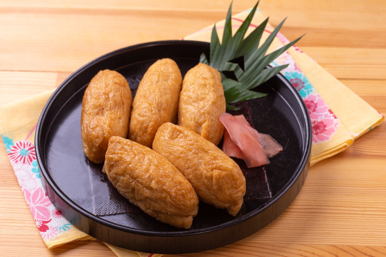 Inari sushi in a black bowl with a leaf