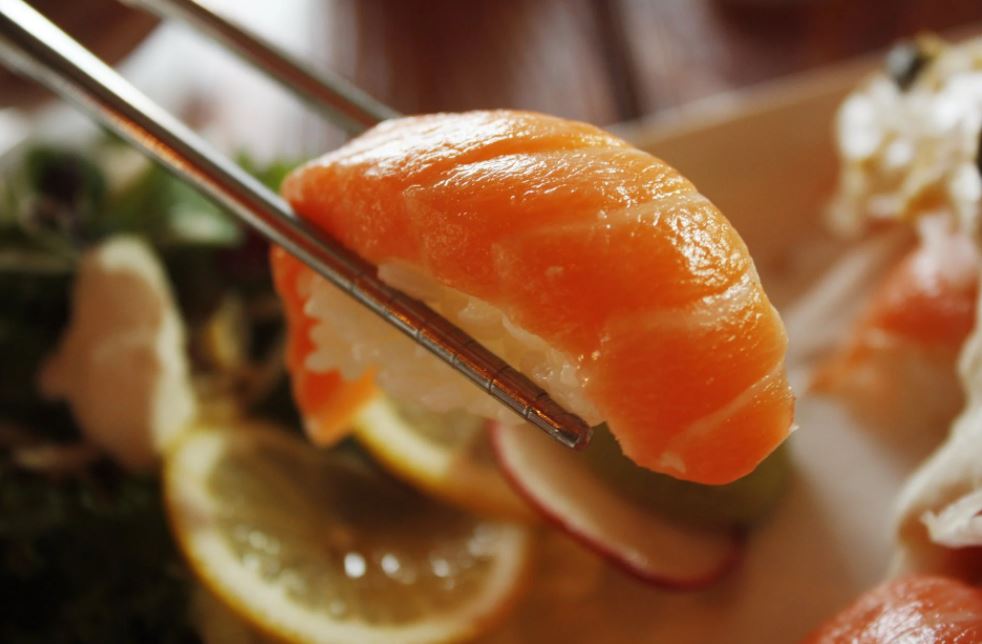 a slice of sushi picked up by chopsticks