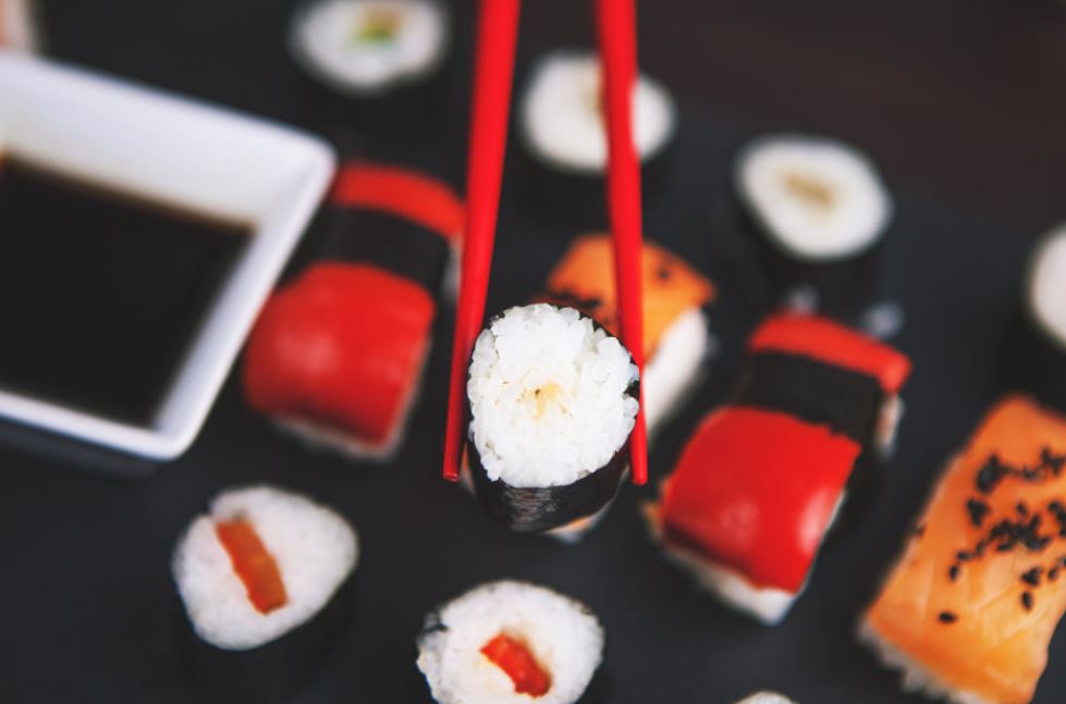 a sushi picked up by chopsticks, a plate of sushi in the background