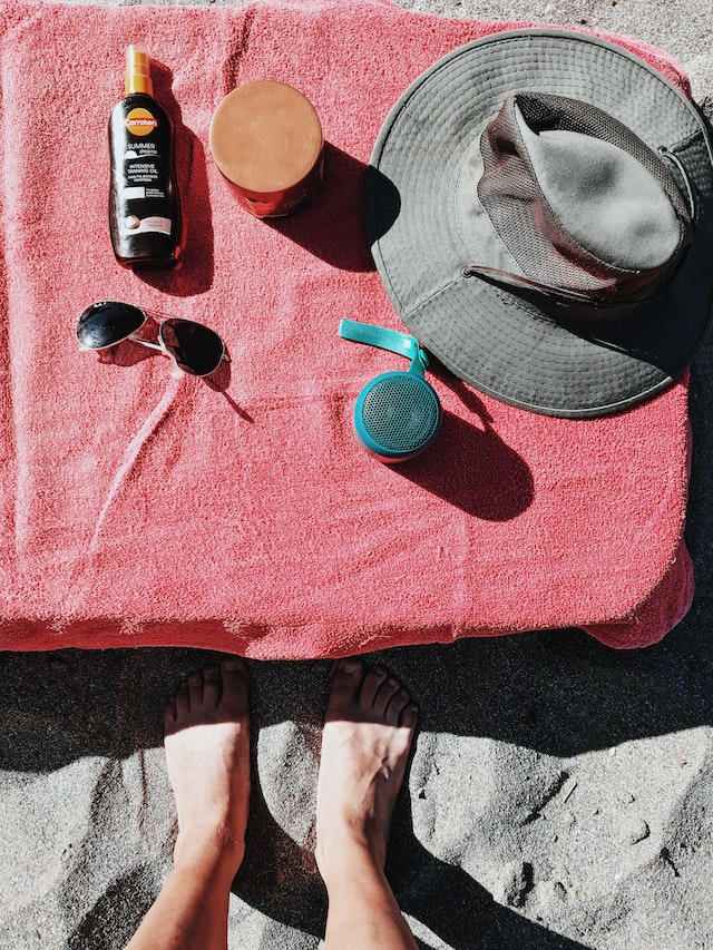 A person’s legs with summer essentials on a beach