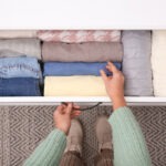 A woman holding a drawer full of folded clothes